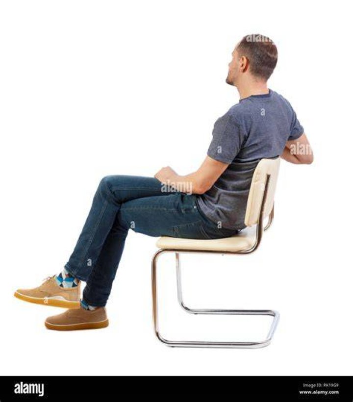 a man sitting in a chair with a guitar on his lap and wearing a hat